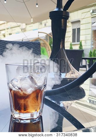 Glass Of Cold Whiskey With Hookah On Table.
