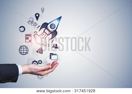 Hand Of Businessman Launching Startup Rocket Over Gray Wall Background. Concept Of New Business Proj