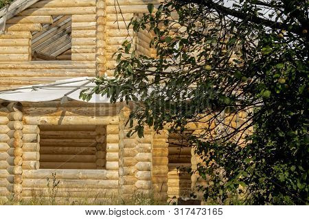 Construction Of A Wooden Residential Building. Walls Made Of Round Logs. Main Facade With Bay Window