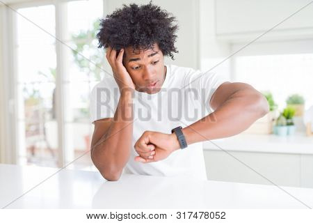 Young african american man wearing casual white t-shirt sitting at home Looking at the watch time worried, afraid of getting late