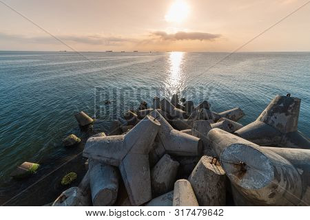 Beautiful Sunset Seascape. Breakwaters Tetrapods Ashore Of Pier. Cargo Ships On The Horizon. Travel 