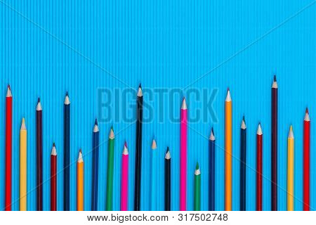 A Bunch Of Crayons On A Blue Background, Shot From Above , Aligned At The Bottom Left, Closeup.