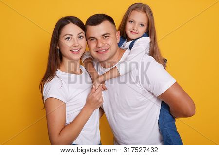 Portrait Of Happy Parents, Daddy Carries Their Beautiful Daughters On His Back. Lovely Family Of Thr