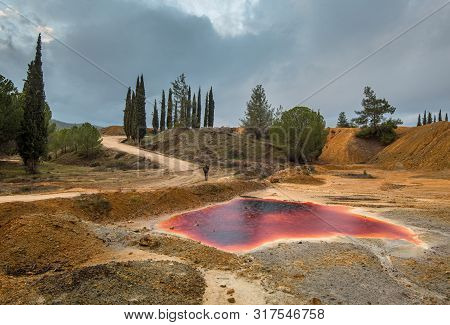 Unrecognizable Man Walking On Near A Lake With Red Polluted Toxic Water Of An Abandoned Copper Mine 