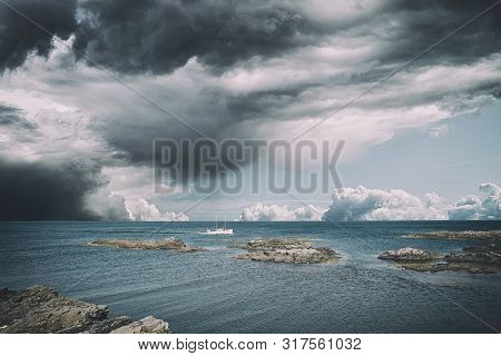 Small Boat In Dramatic Cloudy Weather On The Sea Sailing Close To Cliffs On The Shore
