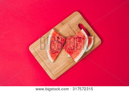 Slices Of Ripe Juicy Watermelon On A Wooden Board And Heart Shape Isolated On A Red Background. The 