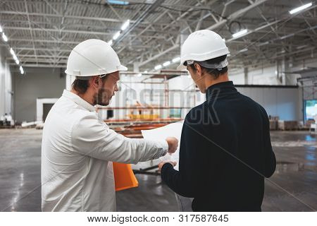 Building Industry. Young Engineer Discussing With Building Worker On Construction Site. Industrial E
