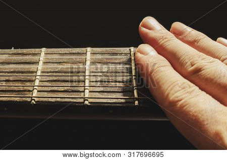 Fingers Muffling The Sound Of The Strings Of An Old Acoustic Guitar, Isolated On A Black Background.