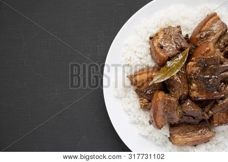 Homemade Filipino Adobo Pork With Rice On A White Plate Over Black Surface, Top View. Flat Lay, Over