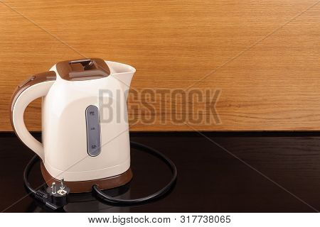 Beige And Brown Color Plastic Cordless Electrical Kettle On The Wood And Black Mirror Background Wit