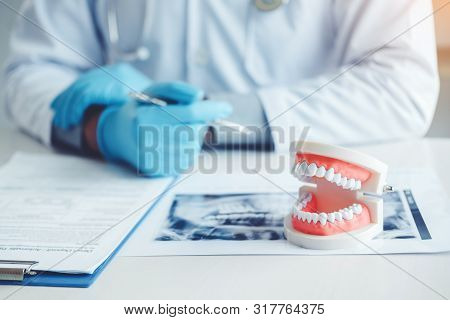 Dentist Consulting With Patient Presenting Results On Dental X-ray Film About The Problem Of The Pat