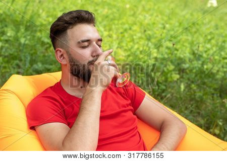 A Young Man With A Beard Lies On An Orange Lamzac Inflatable Sofa And Drinks A White Alcoholic Drink