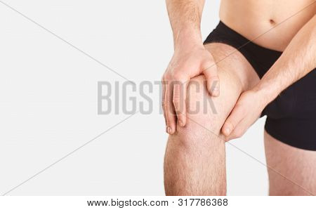 A Man In Underwear Holds His Knee With A Hand On A Gray Background.