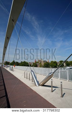 The Hoge Brug, A Pedestrian And Bicycle Suspension Bridge Over The Meuse River, With The Basilica Of