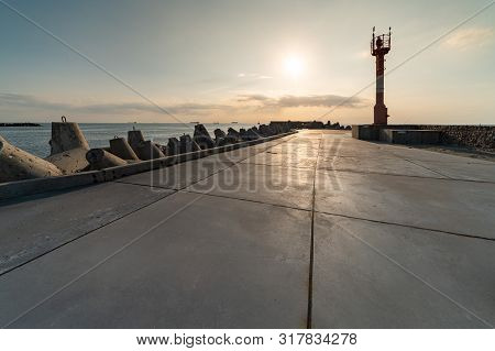 North Pier With Breakwaters, Sunset Seascape. Modern Lighthouse In Sunlight. Tetrapods Along Edges O