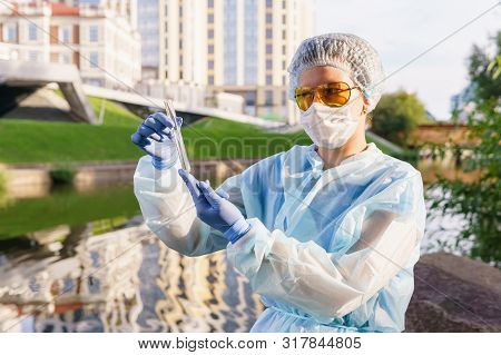 Female Ecologist Or Epidemiologist Visually Assesses The Quality Of Water In An Urban River, Looking