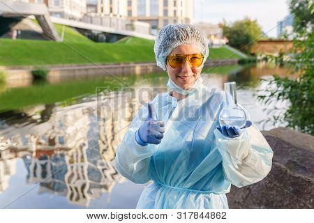 Female Ecologist Or Epidemiologist Gestures For Excellent Quality Of City Water, Holding A Flask In 