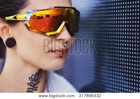 Portrrait Of Girl In Big Toned Glasses And With Piercing Over Interesting Wall With Dots.