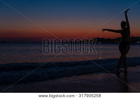 Insatiable Beautiful Stands On The Beach On A Dim Fog From Sunset In A Warm Sea With A Silhouette