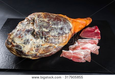 Traditional Spanish jamon Iberico dry aged haunch of a duroc pork as closeup offered on black background 