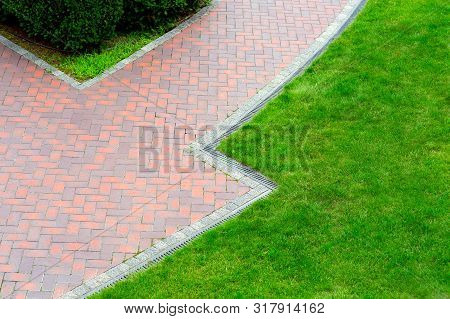 A Footpath Made Of Stone Red Tiles With A Border Of Gray Stone And A Lattice Of A Drainage System Fo