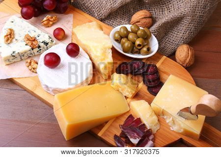 Assortment Of Cheese With Fruits, Grapes, Nuts And Cheese Knife On A Wooden Serving Tray.