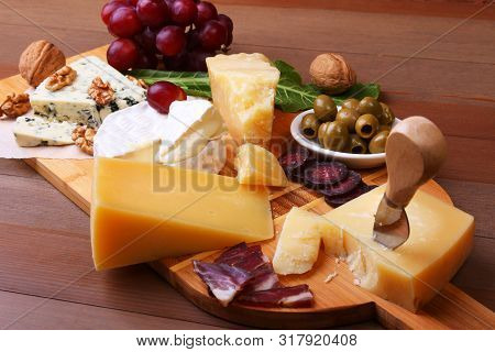 Assortment Of Cheese With Fruits, Grapes, Nuts And Cheese Knife On A Wooden Serving Tray.
