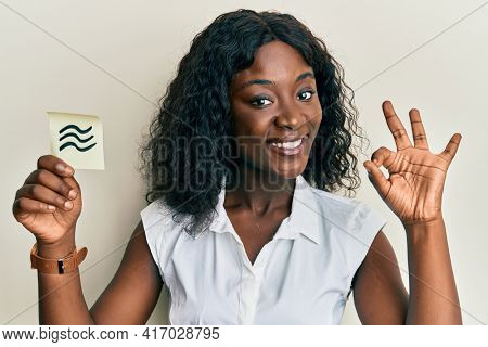 Beautiful african young woman holding paper with aquarius zodiac sign doing ok sign with fingers, smiling friendly gesturing excellent symbol 