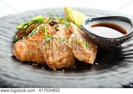 Teppanyaki Style Salmon - Grilled Salmon Fillet with Soy Sauce and Vegetables. Japanese Teppanyaki Salmon Steak garnished with lemon and green beans leaf. Black asian plate close up view