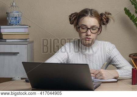 Autiful Serious Teenage Girl In Glasses Is Engaged Online On A Laptop. A Teenage Girl Looks At A Lap