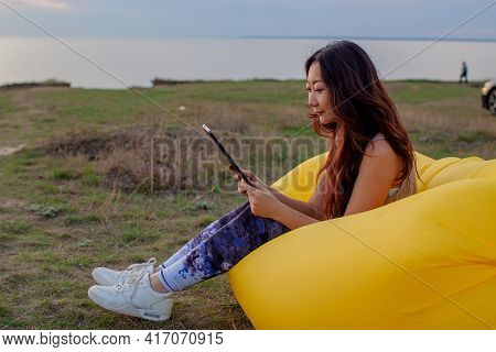 Asian Woman Lying On Inflatable Sofa Lamzac While Resting With Laptop At Sunset On The Mountain