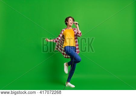 Full Size Photo Of Optimistic Cute Lady Singing In Microphone Wear Jeans Shirt Sneakers Isolated On 