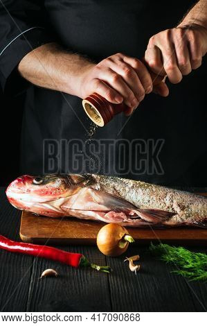 The Chef Prepares Fresh Fish Bighead Carp Sprinkling Pepper. Preparing To Cook Fish Food. Working En