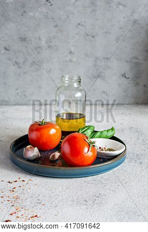 Fresh Ripe Vegetables (garlic Tomatoes) With Basil Leaves, Spices And Olive Oil On A Plate On A Gray