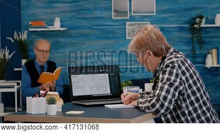 Senior Woman Architect Analysing Digital Prototype With Plans From Laptop