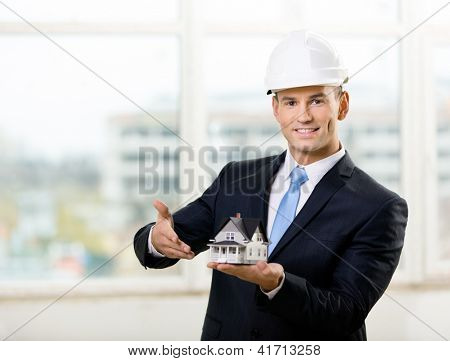 Engineer in white hard hat pointing at small model house. Concept of real estate