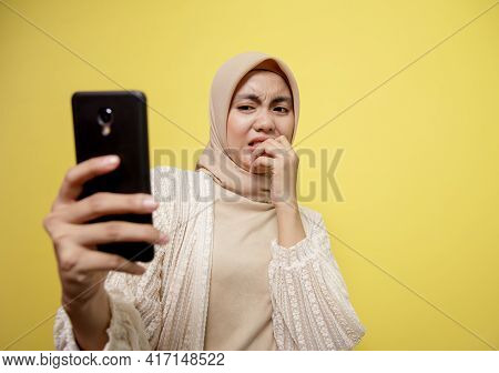 Young Woman Wearing Hijab With An Expression Disgusted While Looking Her Phone