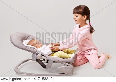 Little Cute Girl With Pigtails Playing With Her Newborn Sister While Sitting With On Floor Isolated 
