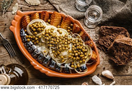 Fried Potatoes With Herring Fish Slices, Canned Green Peas And Onions In Plate On Wooden Rustic Tabl