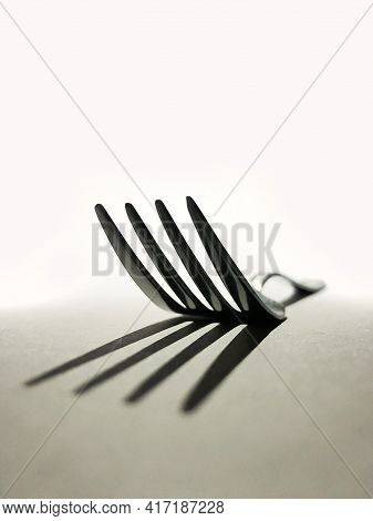 Vertical Conceptual Low Angle View Image Of A Single Silver Four Tines Dinner Fork, Casting Shadow O