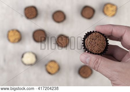 Hand Holding Typical Brazilian Brigadeiros Over Unfocused Brigadeiros On The Background.