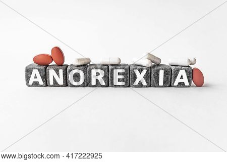 Anorexia The Word On Stone Cubes. Cubes Stand On A White Surface, Many White And Red Pills. Medicine