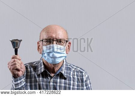 Old Bald Man With Glasses And Medical Mask With Bell In His Hand. Copy Space.