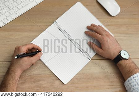 Left-handed Man Writing In Notebook At Wooden Table, Top View