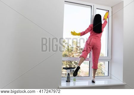 Young Woman Cleaning Windows In Building. Housekeeping.