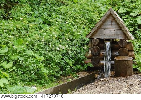 Pure, Cold, Wellspring Water Flows In The Mountains From The Source In The Form Of A Wooden House In