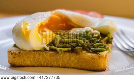 Fresh Homemade Delicious Sandwich With Avocado And Poached Egg And Cut Yolk On A White Plate Closeup