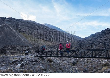 Tongariro New Zealand - March 27 2021; Trampers Cross Small Bridge In Morning Light Framed By Volcan