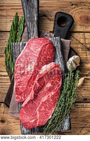 Raw Shoulder Top Blade Beef Meat Steaks On A Wooden Butcher Board With Herbs. Wooden Background. Top