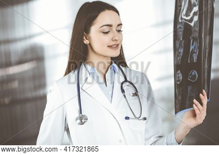Professional Young Woman-doctor Is Looking At Her Patients Roentgenogram. Physician At Work In A Cli